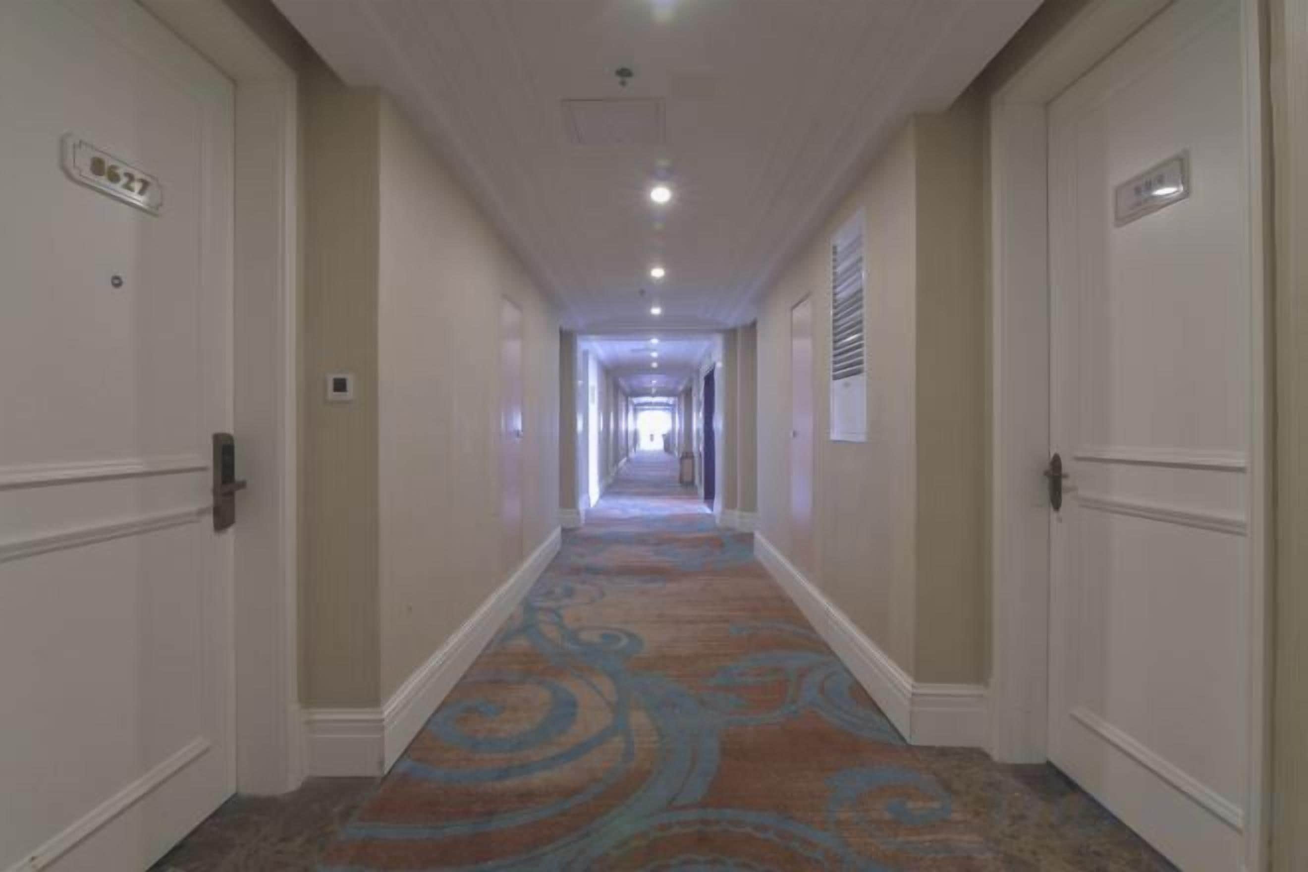 A hotel hallway with carpeted floors, doors on both sides, and a light fixture on the ceiling.
