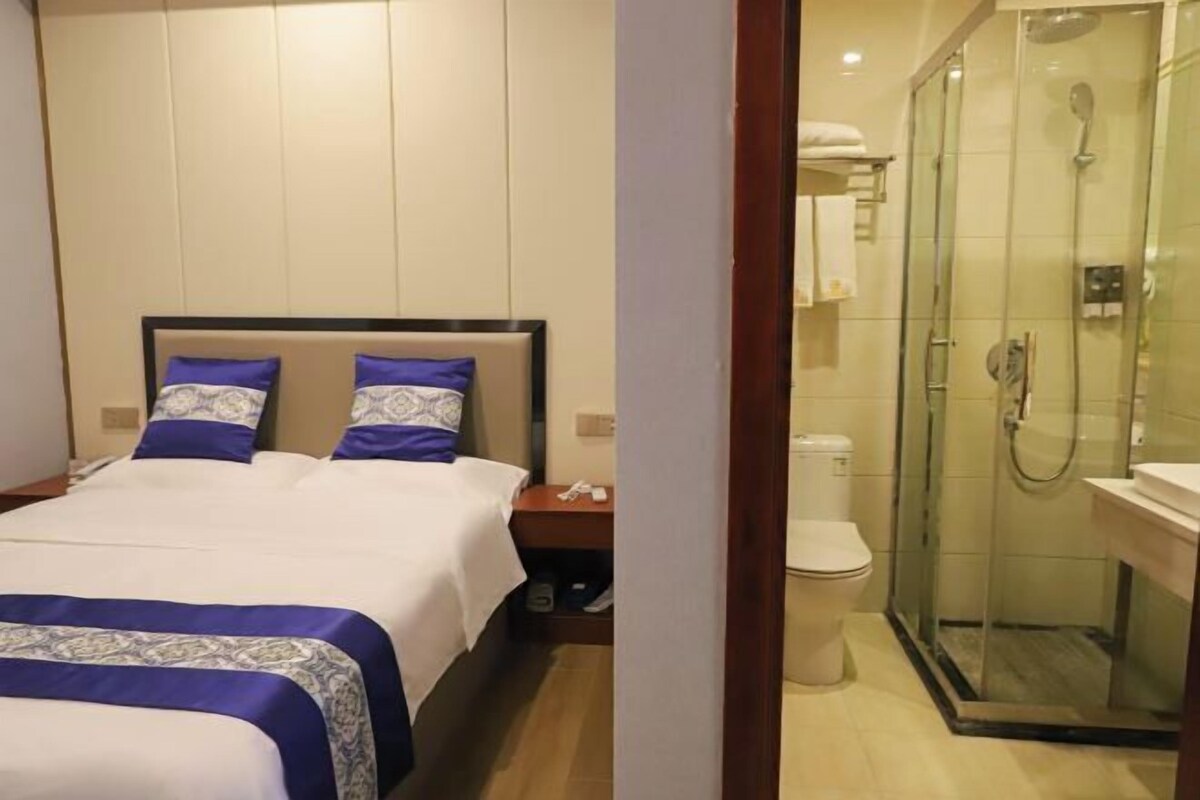 Una habitación de hotel con cama, mesita de noche, baño con cabina de ducha de vidrio y un inodoro.