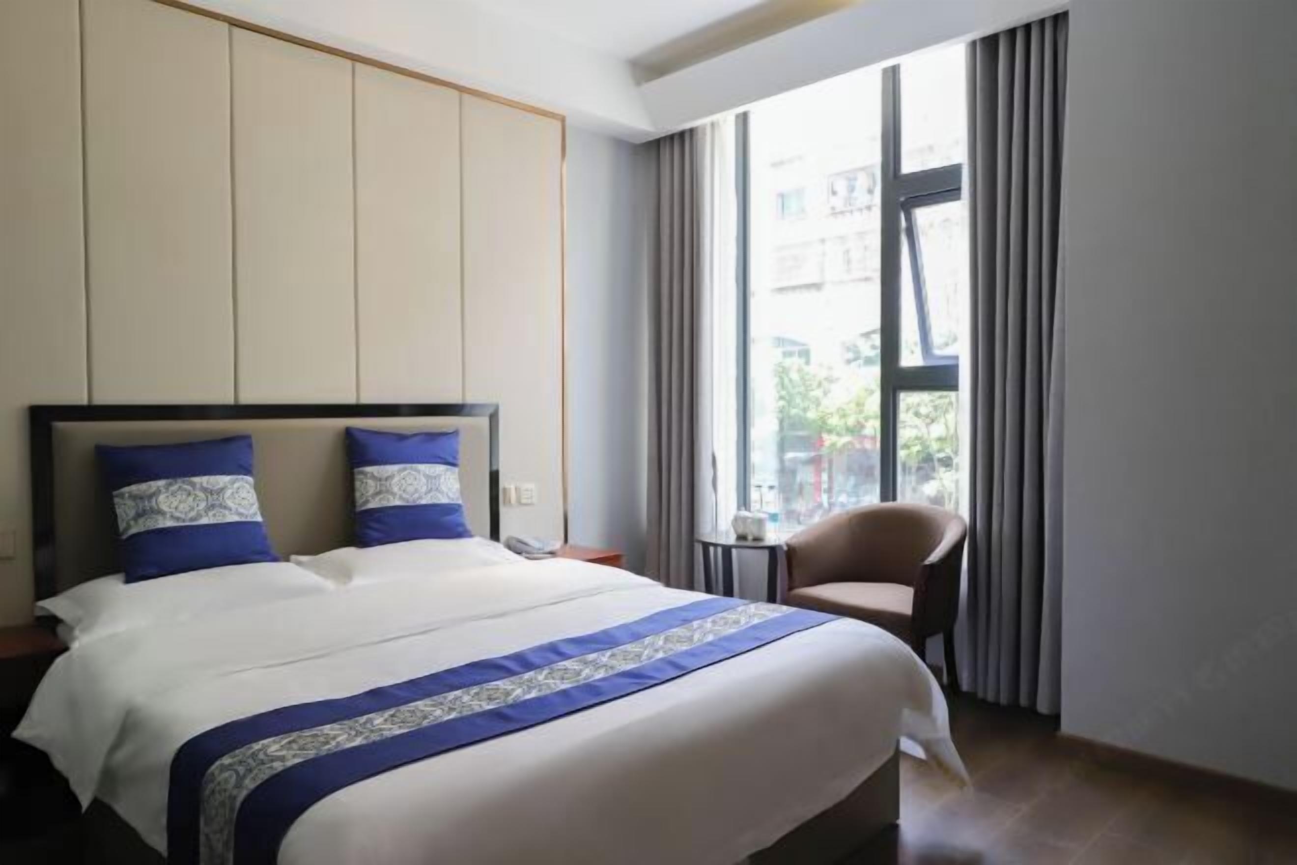 A hotel room with a large bed, a chair, a small table, and a window with curtains.