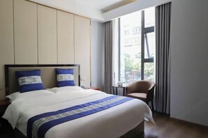 Une chambre d’hôtel avec un grand lit, une chaise, une petite table et une fenêtre avec des rideaux.