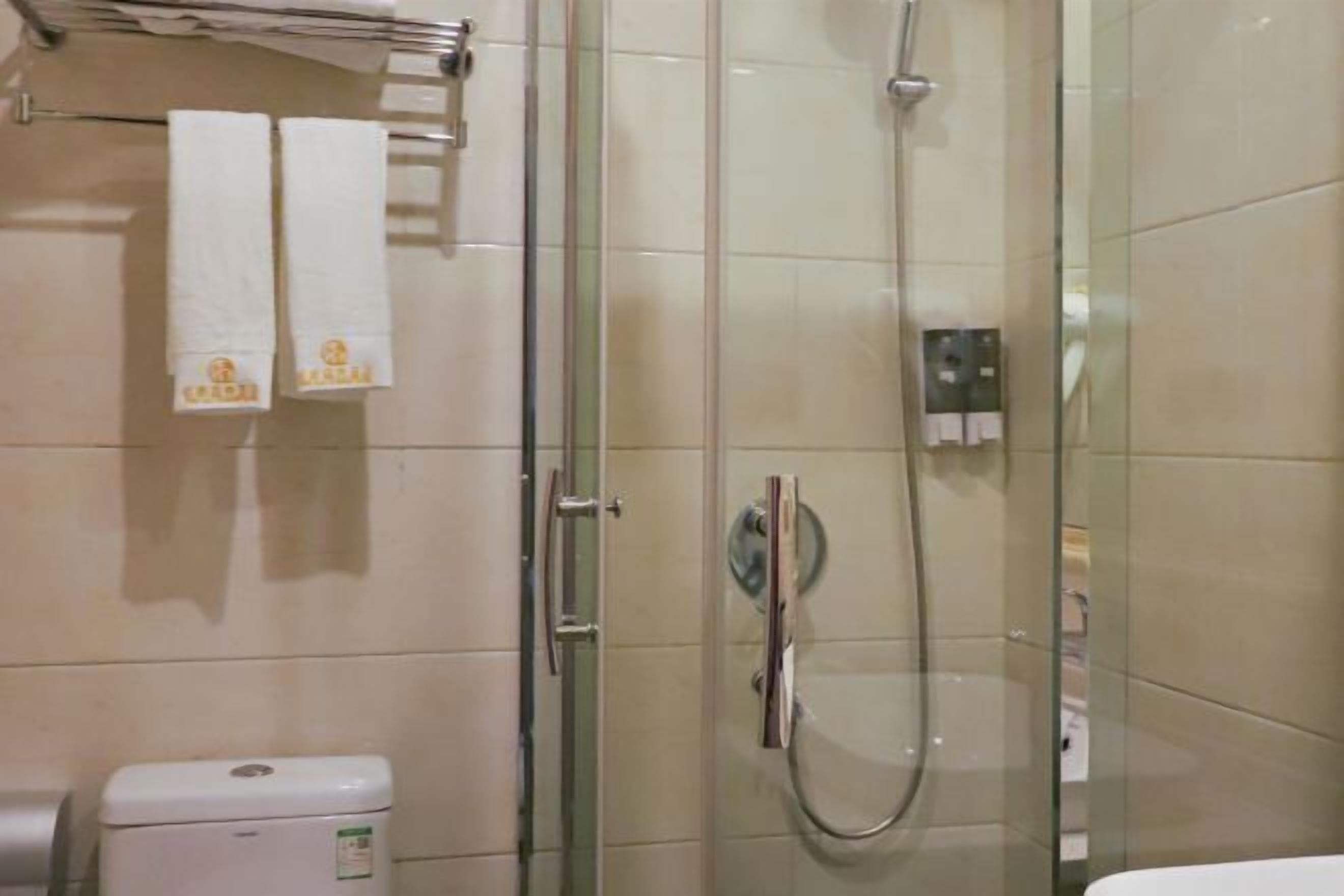Zona de ducha con mampara de vidrio, cabezal de ducha manual, inodoro y toallero con dos toallas.