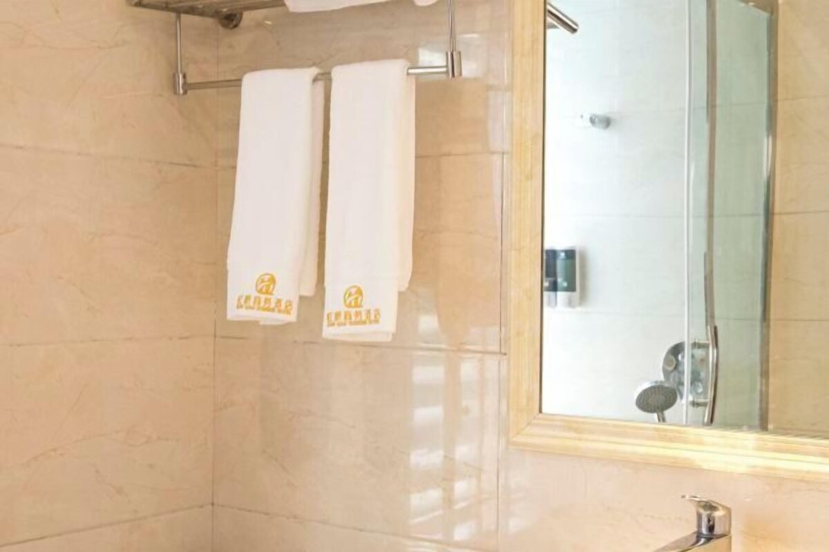 Un baño con dos toallas blancas colgadas en un perchero, un box de ducha de cristal y un espejo sobre el lavamanos.