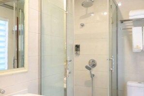 Un baño con ducha de mampara de vidrio, inodoro a la vista y un espejo.