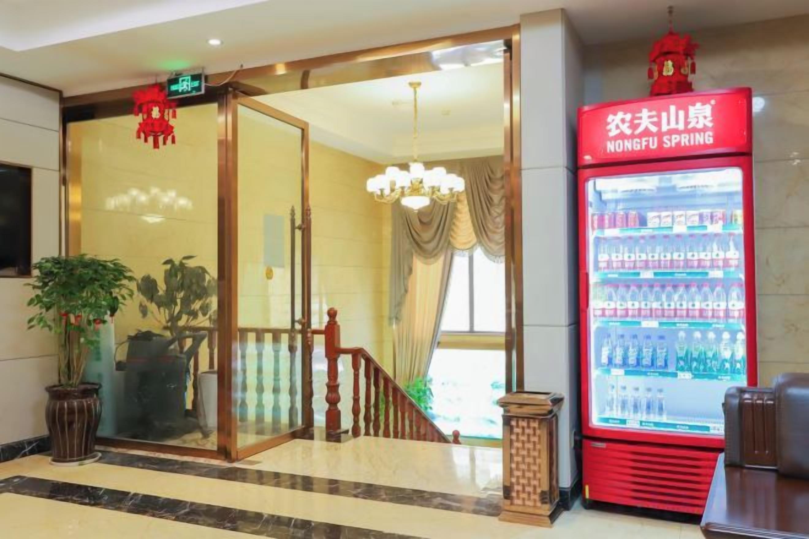 Un vestíbulo de hotel con entrada por puerta de cristal, una máquina expendedora de bebidas roja y un candelabro.