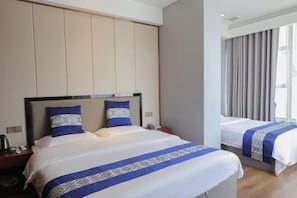 Habitación de hotel con una cama grande, una cama más pequeña y una mesita de noche con un teléfono y una lámpara.