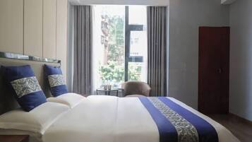 A hotel room with a large bed, a small table, and a wardrobe.