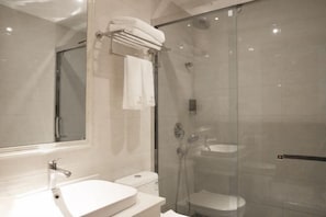 Un baño moderno con ducha de vidrio, un lavamanos blanco y un espejo grande.