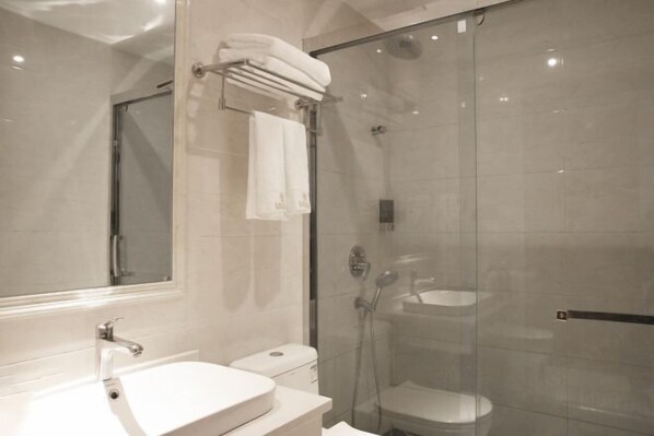 Un baño moderno con ducha de vidrio, un lavamanos blanco y un espejo grande.