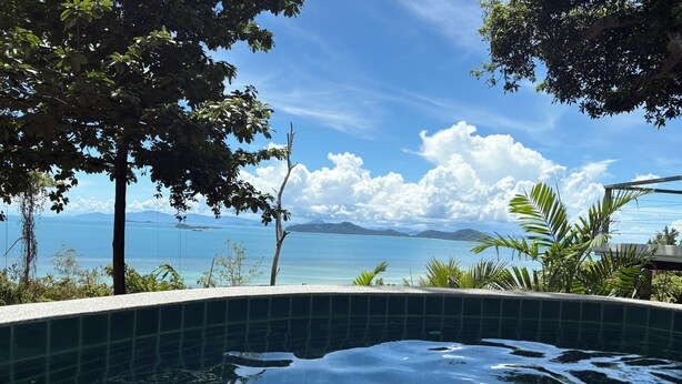 A clear view of a swimming pool with a tiled edge, surrounded by lush greenery and overlooking a body of water with distant landforms. - Koh Samui Villa, Beautiful Pool and Wide Sweeping Sea Views over the Islands  (NAMUANG)
