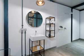 A modern bathroom with a white sink, round mirror, and black shelving unit.