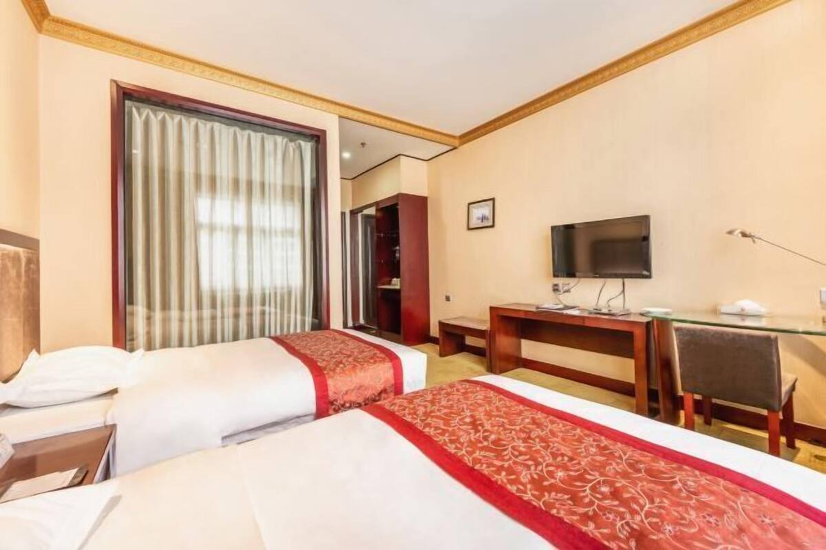 Habitación de hotel con dos camas, un escritorio, un televisor y un ventanal grande con cortinas.