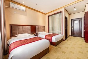 Une chambre d’hôtel avec deux lits, une grande fenêtre avec des rideaux, un appareil de climatisation et un sol recouvert de moquette.
