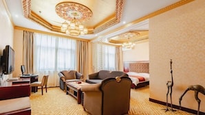 Une chambre d’hôtel avec un tapis à motifs, un canapé, un bureau avec une chaise, une télévision et un lit avec des rideaux.