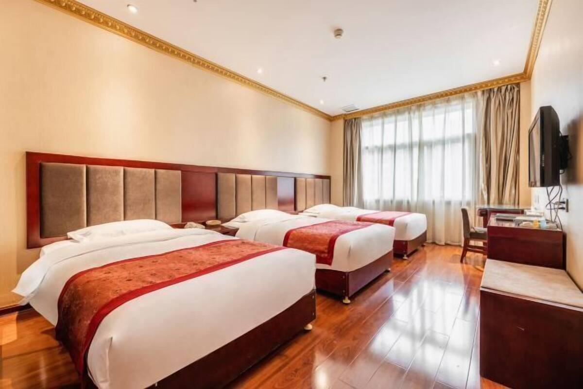 Habitación de hotel con tres camas, piso de madera, escritorio y televisión.