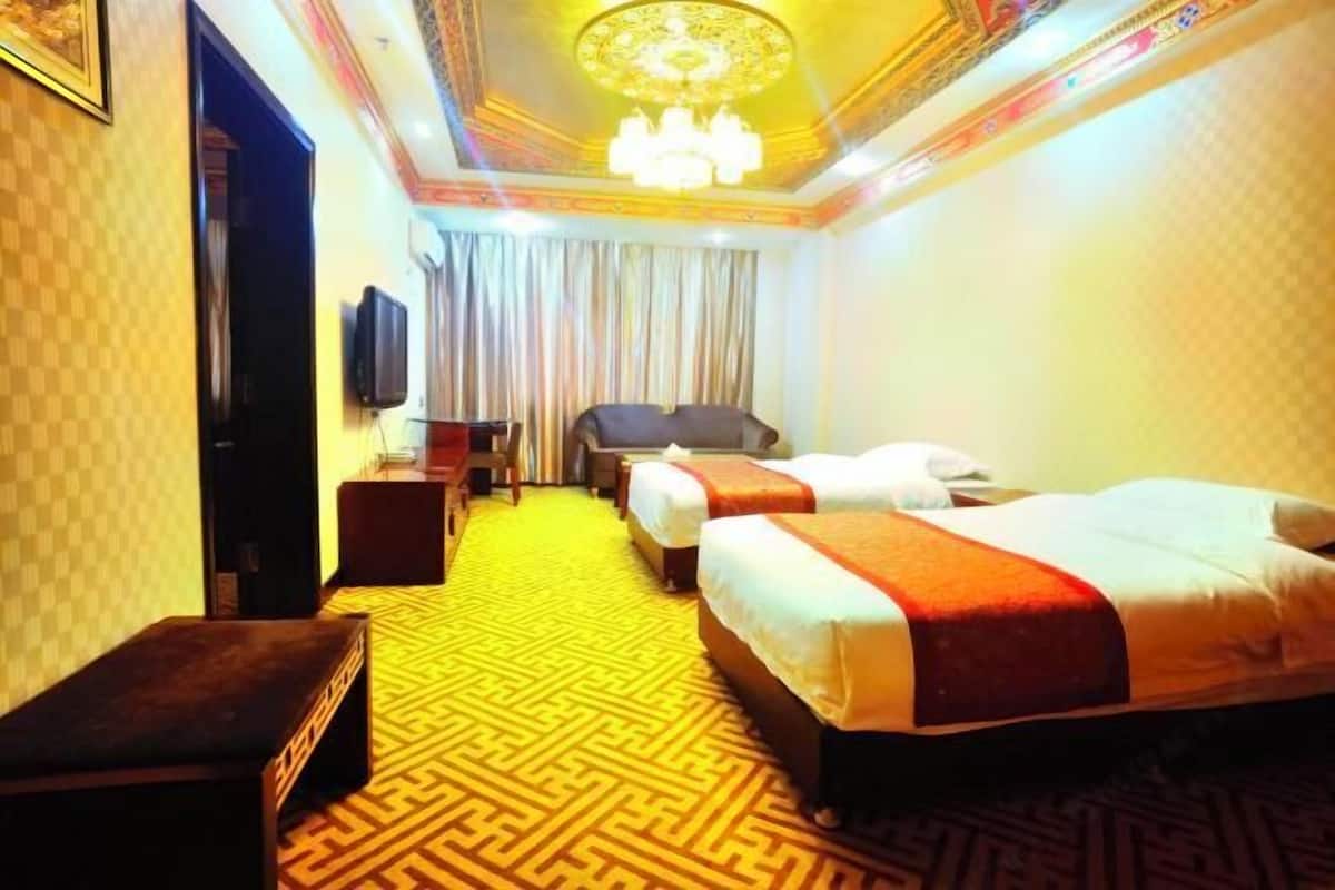 Una habitación de hotel con alfombra a cuadros, una cama con colcha roja y blanca, un escritorio con una silla, un televisor y una araña.
