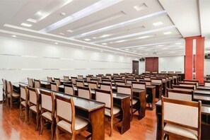 Une salle de conférence avec des rangées de tables et de chaises, une scène et un pilier rouge.