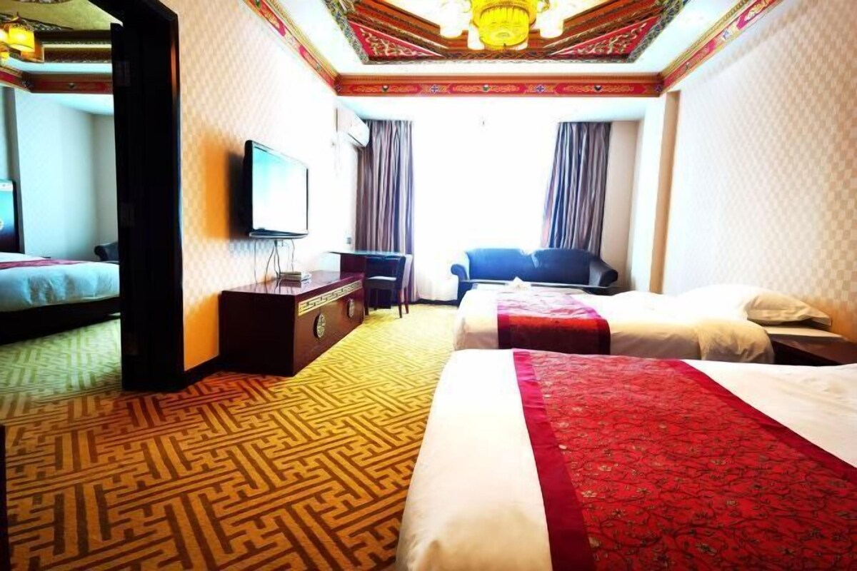 Une chambre d’hôtel avec deux lits, un bureau, une télévision et une moquette à motifs.