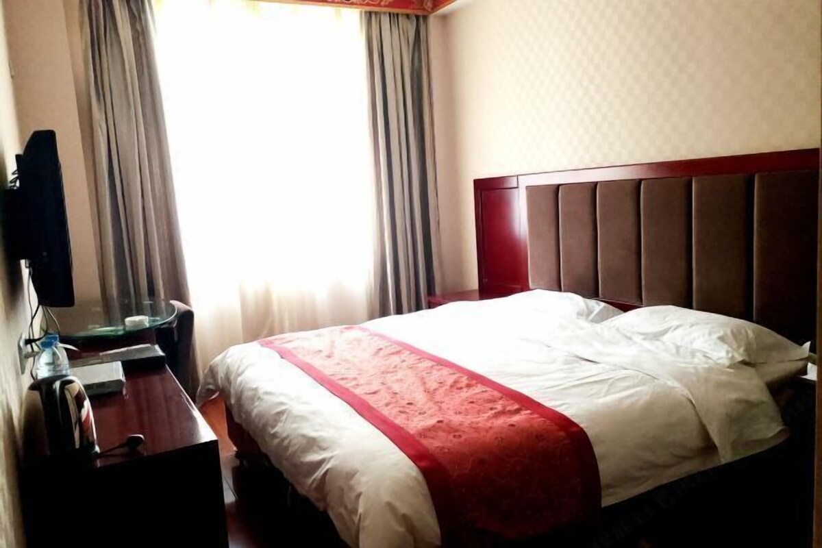Une chambre d’hôtel avec un lit, un bureau, une chaise, une télévision et une fenêtre avec des rideaux.