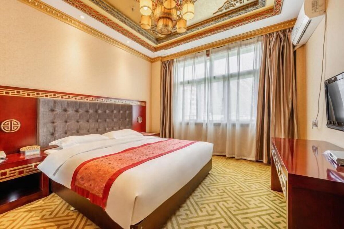 Une chambre d’hôtel avec un grand lit, un bureau, une télévision et une fenêtre avec des rideaux.