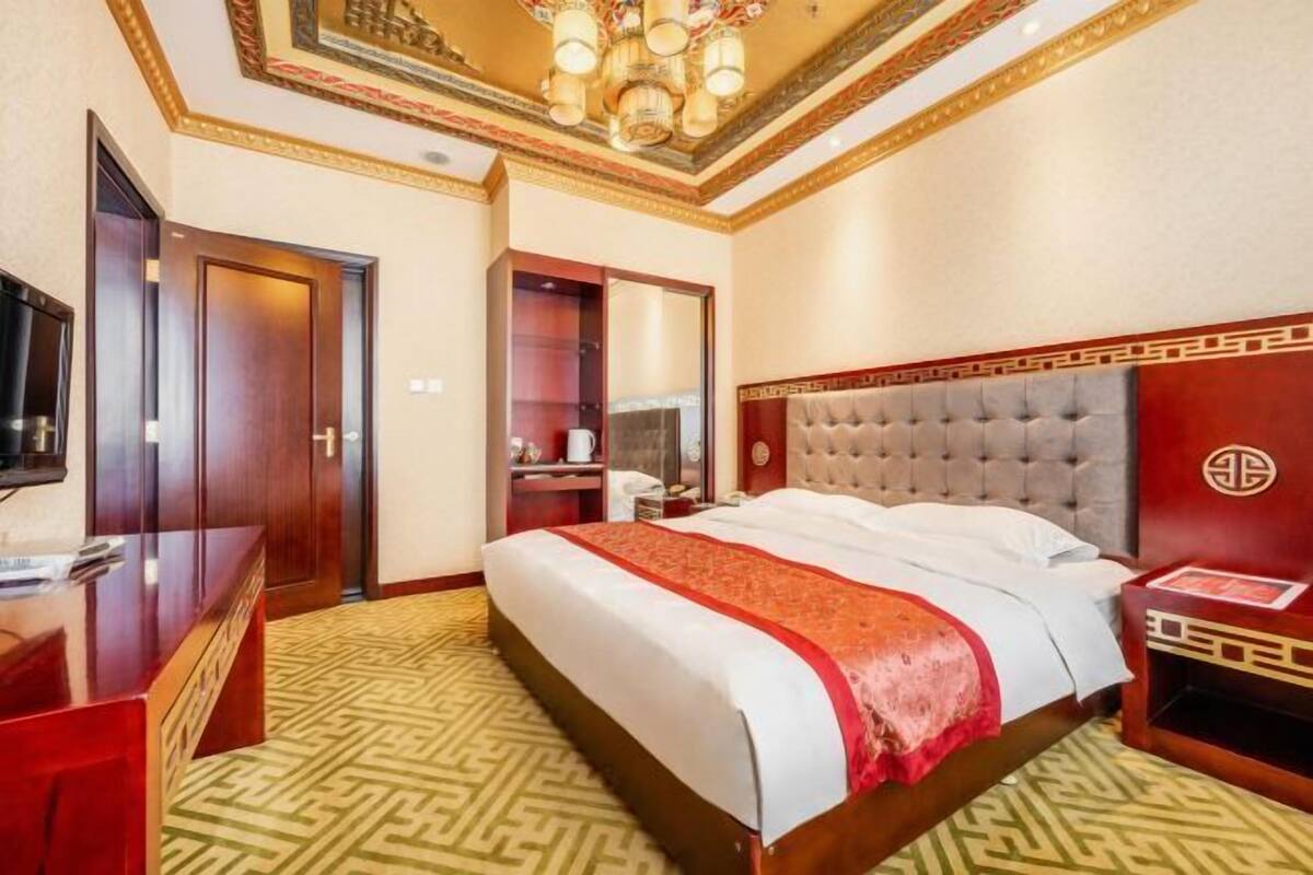 Una habitación de hotel con una cama grande, un escritorio de madera, un televisor y un espejo.