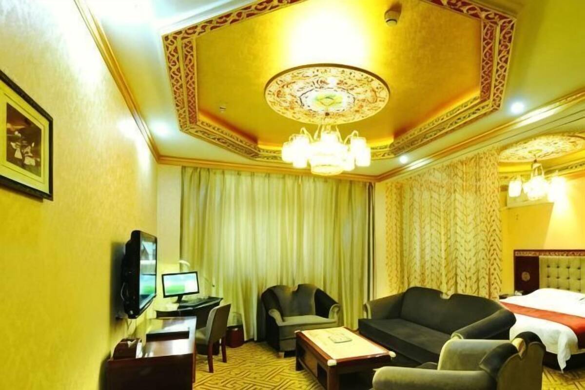 Una habitación de hotel con televisión, escritorio, sofá, sillón, cama y candelabro.