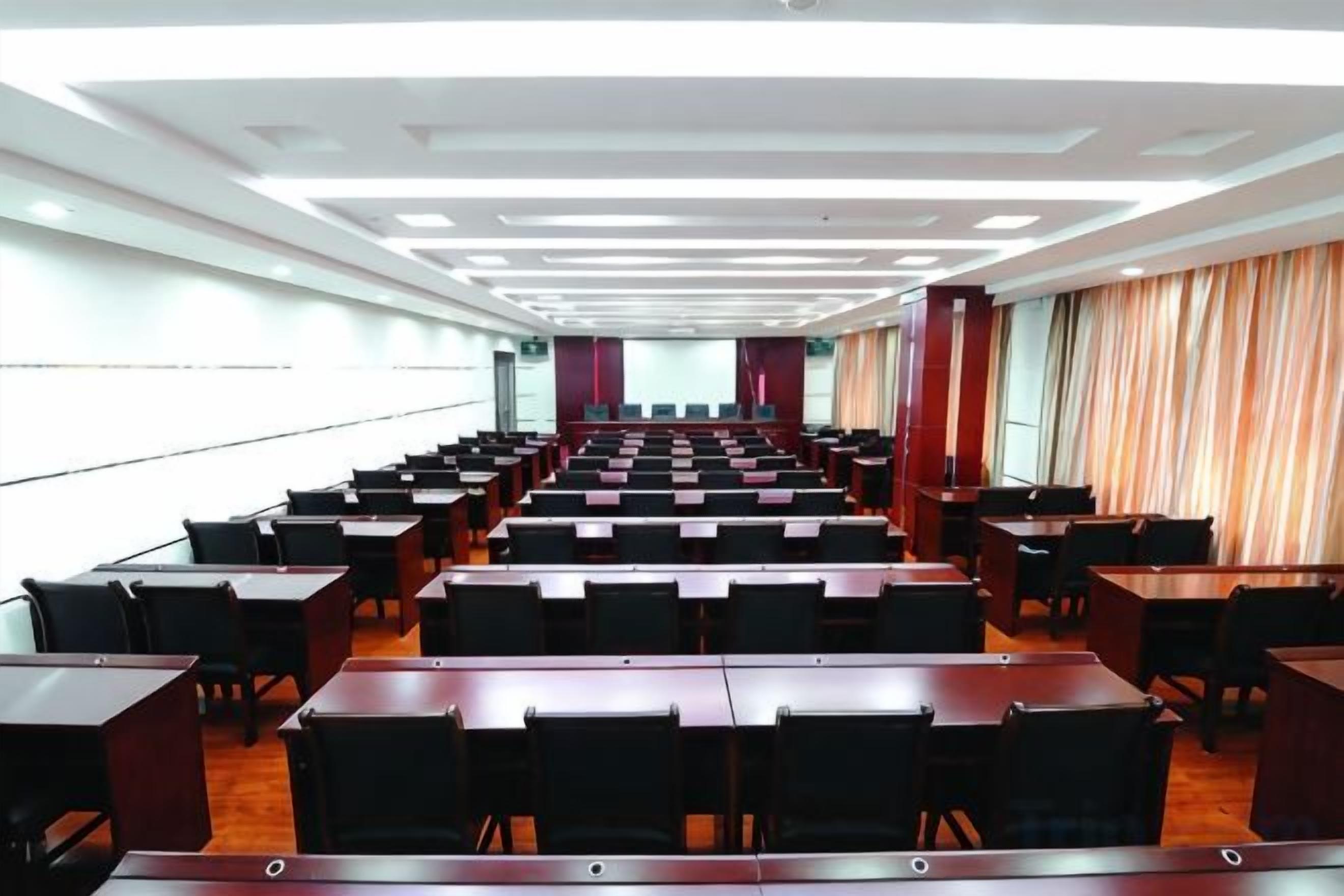 A conference room with rows of tables and chairs, large windows, and a curtain on one side.