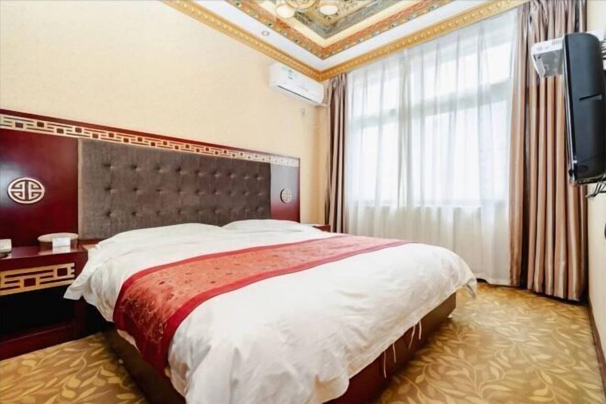 Habitación de hotel con una cama grande, un cabecero decorativo, un televisor montado en la pared y una ventana con cortinas.