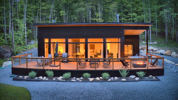 A modern cabin with a deck, large windows, and a fire pit.