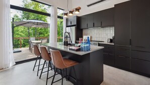 A modern kitchen with a large island, dark cabinets, and a view of the outdoors.