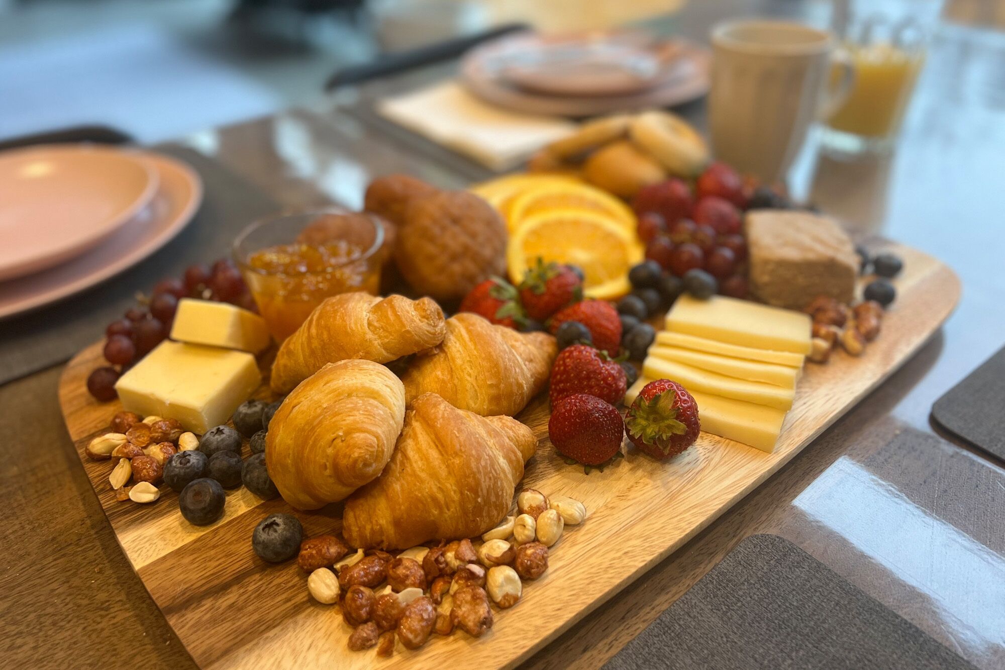 Ein Frühstücksteller mit Croissants, Käse, Erdbeeren, Blaubeeren und Nüssen auf einer Holzplatte.