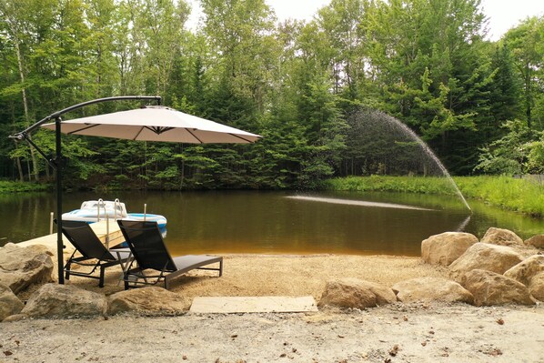 Un cadre idyllique au bord du lac, avec une table et des chaises placées sous un parasol, le tout entouré de rochers et d’une zone sablonneuse.