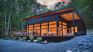 A modern cabin with large windows, a covered deck, and a forest backdrop.