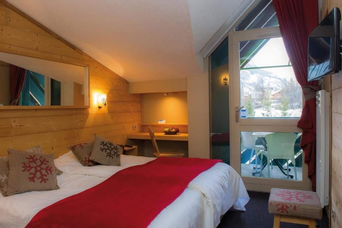 A cozy room with a bed, a desk, and a view of a snowy landscape through a glass door.