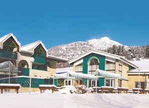Un hôtel composé de plusieurs bâtiments, doté d’une terrasse et offrant une vue sur une montagne enneigée.