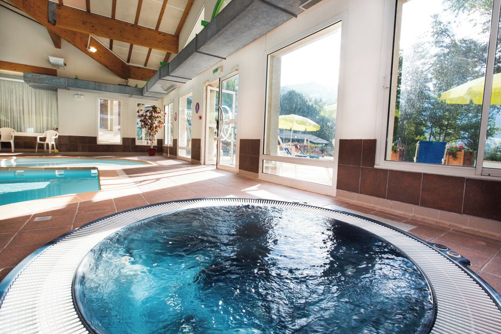 A swimming pool area with a hot tub, large windows, and a view of the outdoors.