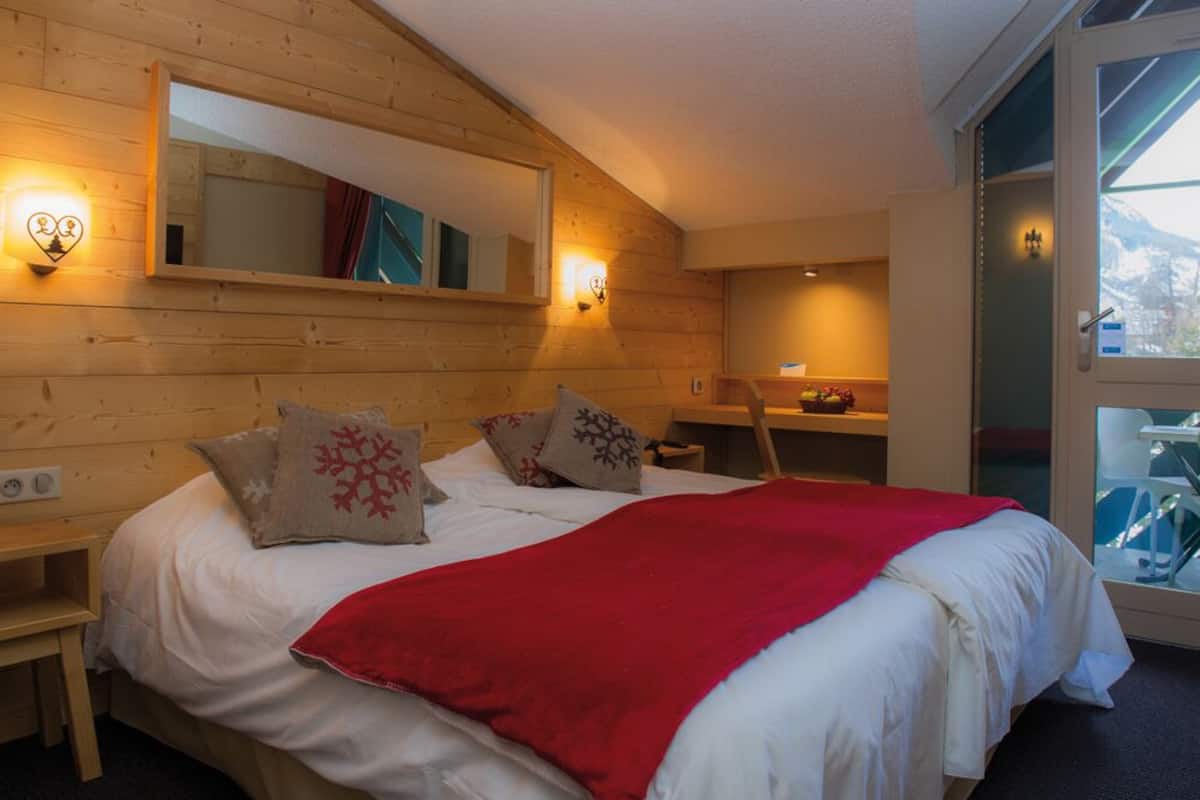 A bedroom with a wooden headboard, a large mirror, and a bed with white bedding and red accents.