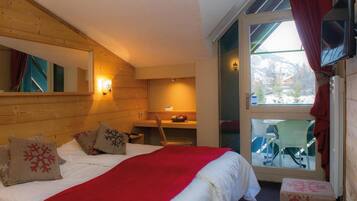 A cozy room with a bed, a desk, and a view of a snowy landscape through a glass door.