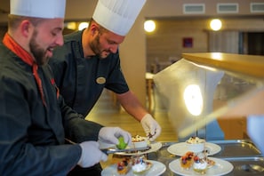 Chefs preparing desserts in a kitchen with stainless steel counters and a warm, well-lit ambiance. - Club Les Alpes Dazur (La Salle-les-Alpes)