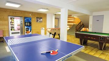 A room with a ping pong table, a pool table, and a vending machine.