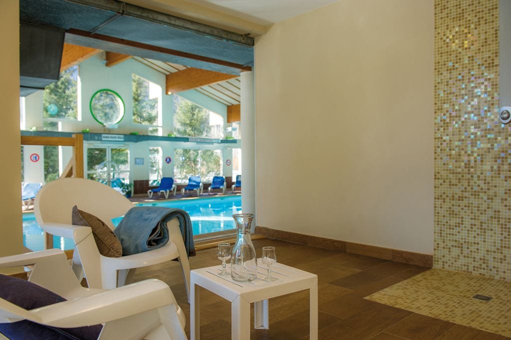 Zona junto a la piscina con sillones de descanso, una mesa con vasos y vistas a la piscina.