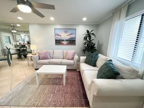 A living room with a white sofa, a coffee table, and a painting on the wall. - NEW Townhouse 3 Min Walk to Beach, 11 pools, backyard (Panama City Beach)