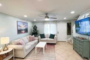 Un salon comprenant deux canapés, une table basse, un téléviseur, un ventilateur de plafond et une porte donnant sur un escalier.