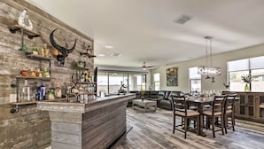 Uma cozinha moderna com ilha central, piso de madeira e área de bar com prateleiras e objetos decorativos.