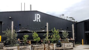 A building with a large 'JR' sign, outdoor seating with umbrellas, and wooden crates labeled 'EMANJAY ORCHIDS'. - Dromana getaway with a view, air con and wi-fi. (Dromana)