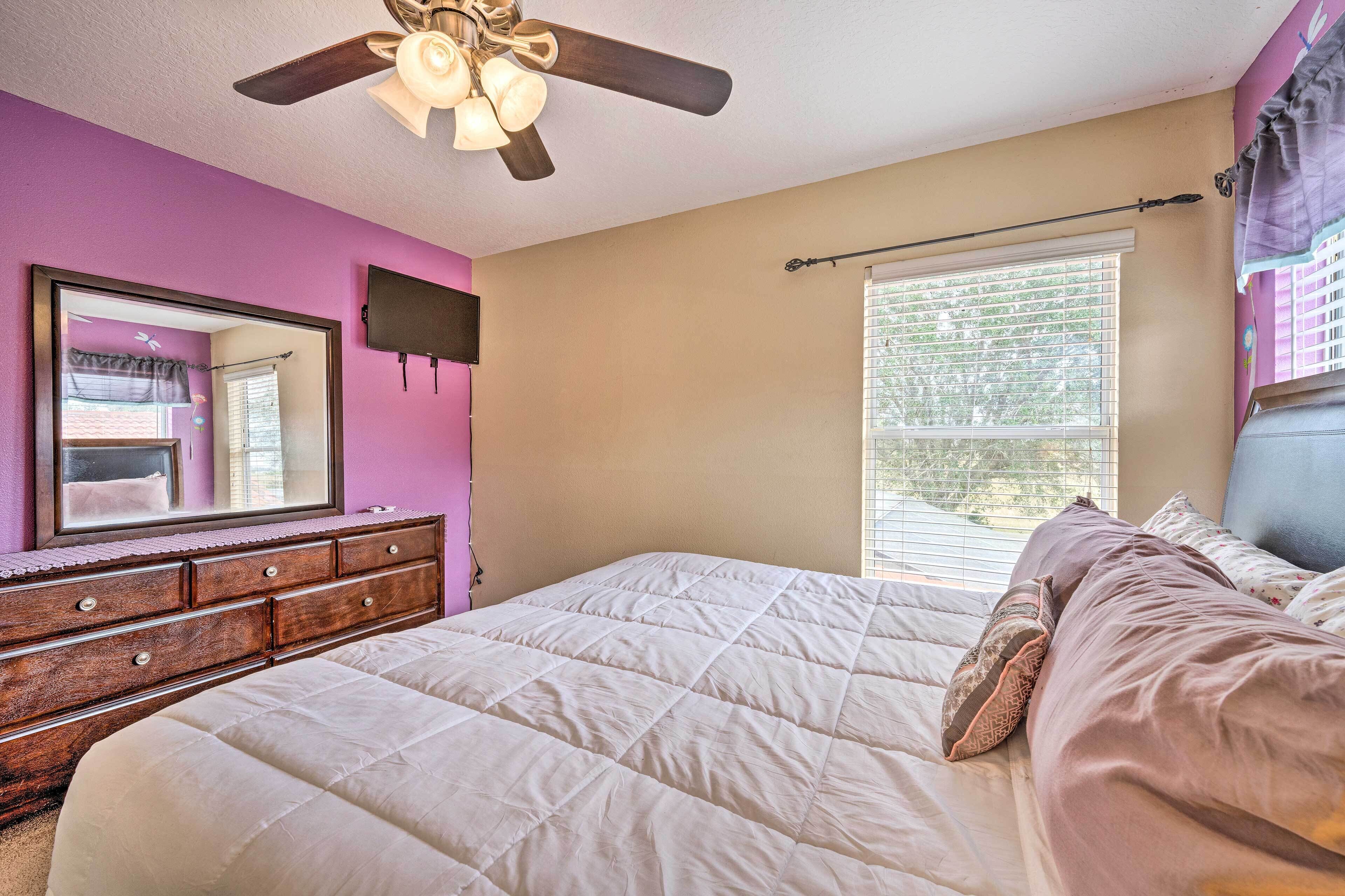 Une chambre à coucher comprenant un lit, une commode, un ventilateur de plafond et une fenêtre avec des stores.