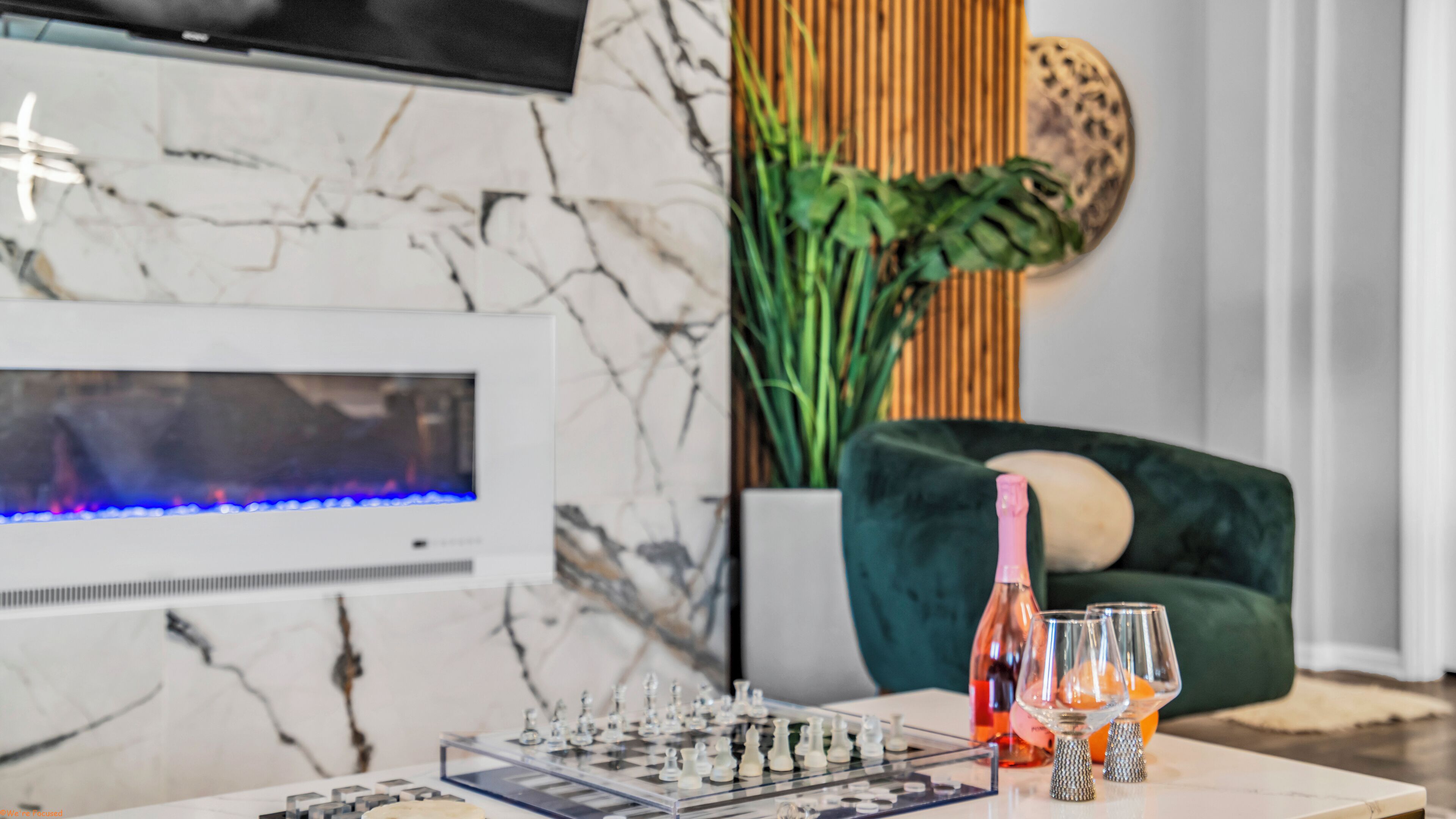 A living room with a marble wall, a flat-screen TV, a chessboard, and a green sofa.
