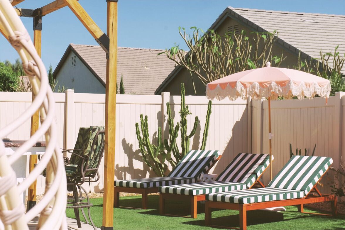 A backyard with two striped lounge chairs, a wooden pergola, a pink umbrella, and cacti.