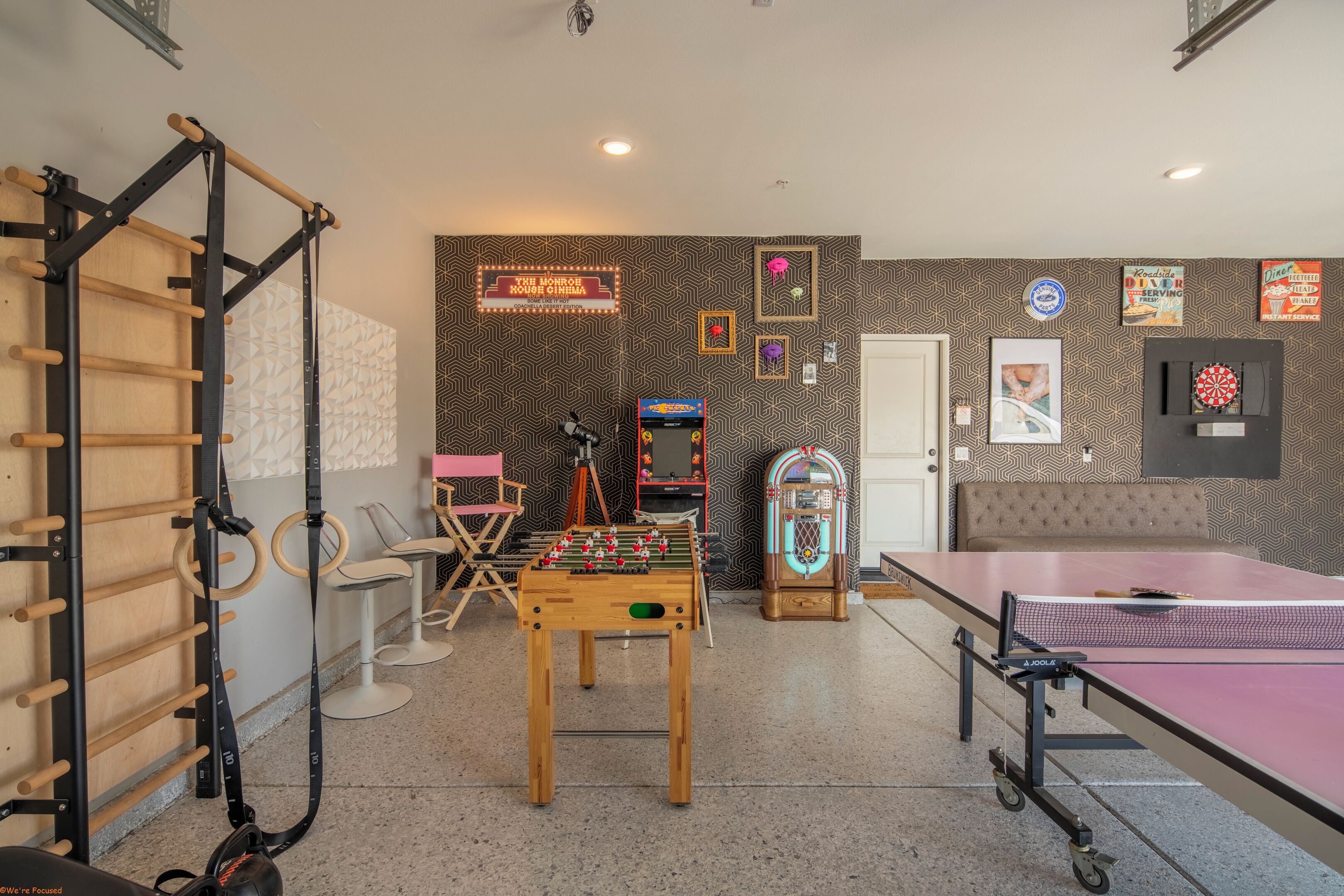 Una stanza con un tavolo da calcio balilla, un tavolo da ping pong, una sbarra per trazioni e una parete con diversi addobbi.