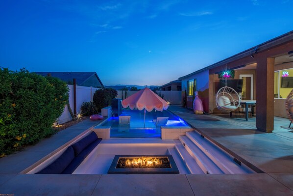 A pool area with a fire feature, seating, and a covered section.