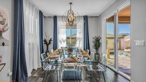A dining area with a glass table and chairs, blue curtains, and a chandelier.